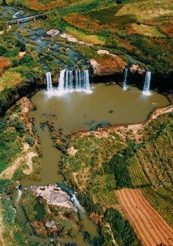 Stunning aerial view of cascading waterfalls surrounded by lush greenery and farmland.