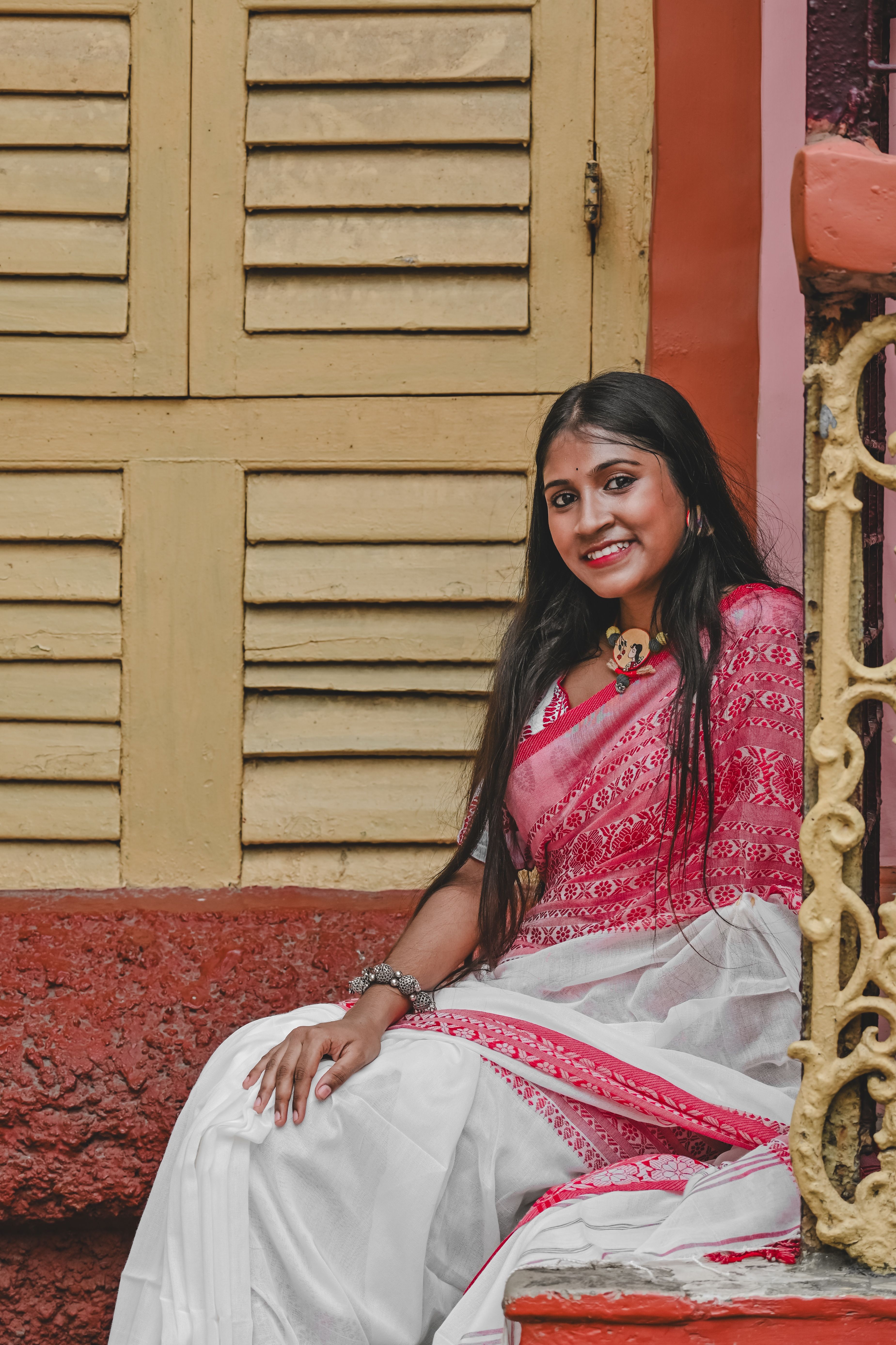 Woman in elegant red and white saree sitting in a colorful Kolkata setting.