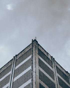 Low-angle photo of a tall concrete building against a dramatic cloudy sky, highlighting urban architecture.
