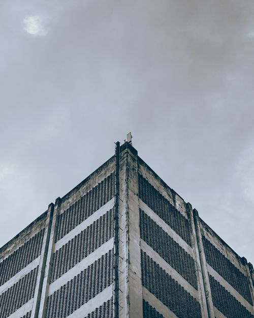 Free Low-angle photo of a tall concrete building against a dramatic cloudy sky, highlighting urban architecture. Stock Photo
