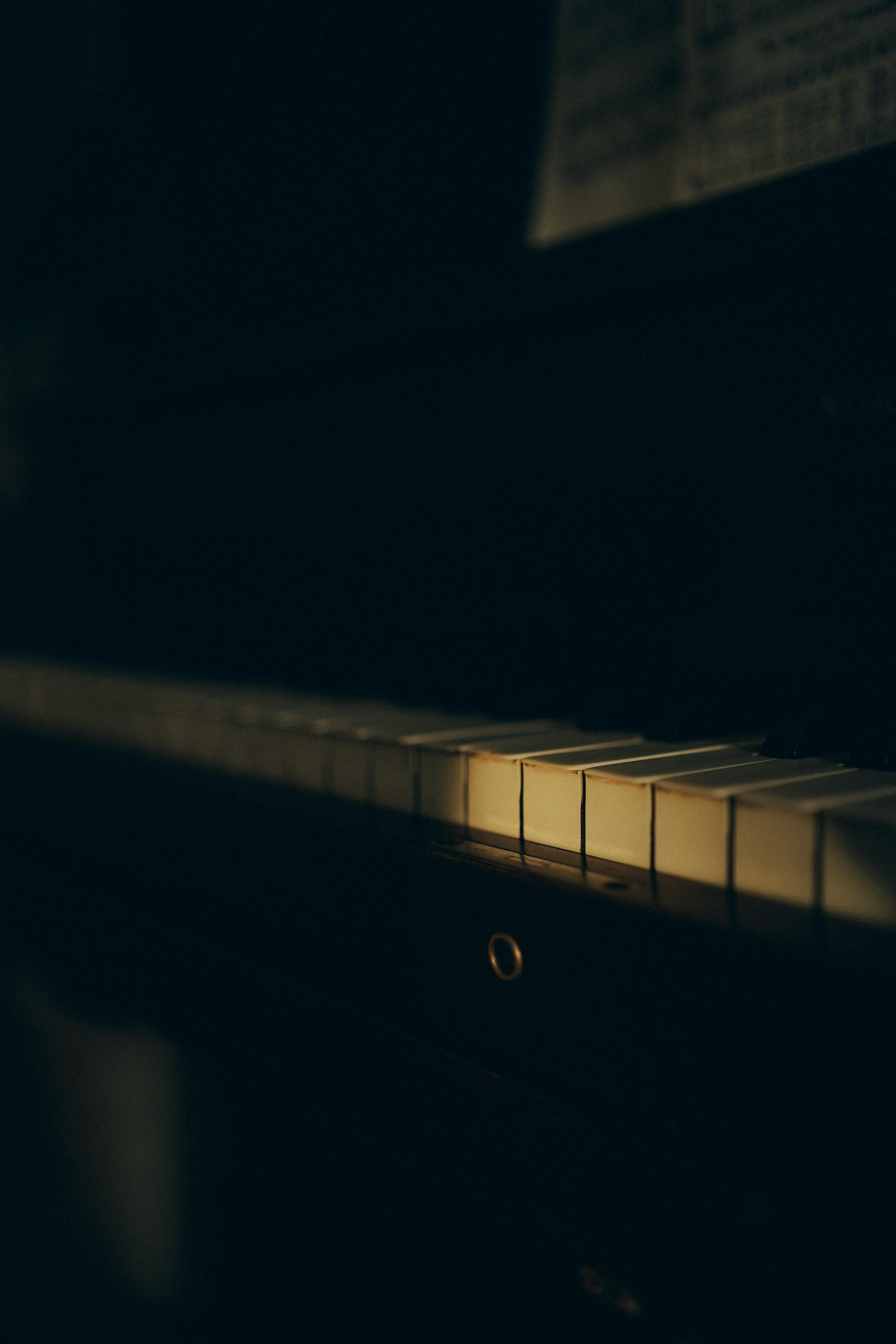 Gratuit Un gros plan maussade des touches d'un piano doucement éclairées dans une pièce faiblement éclairée. Photos