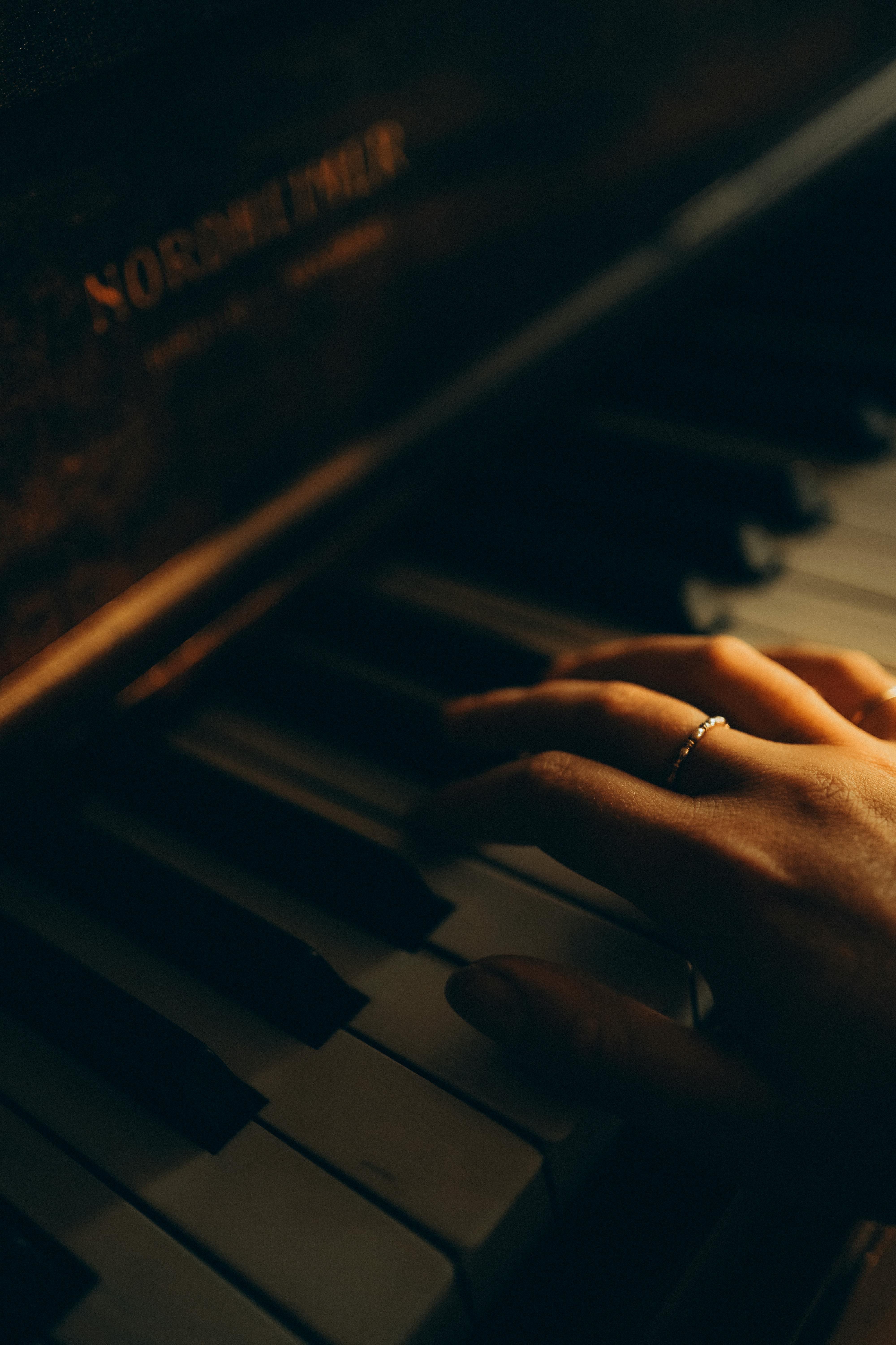 A close-up, warm-toned image of a hand playing piano keys, evoking a moody atmosphere.