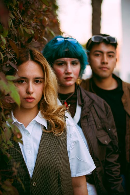 Free Three stylish young adults pose outdoors against a leafy backdrop. Vibrant and modern. Stock Photo