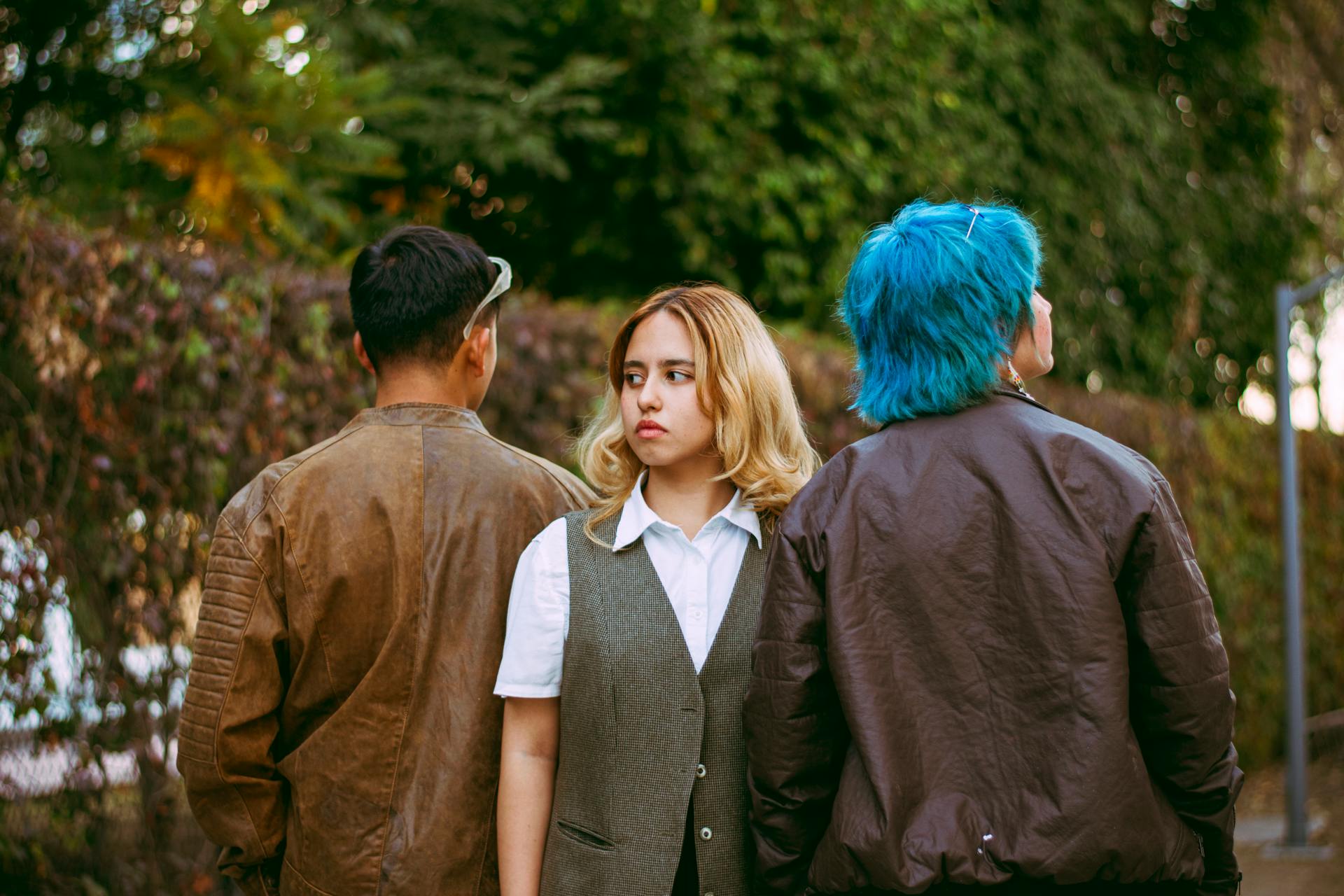 Three stylish friends with unique hairstyles socializing outside in a natural setting.