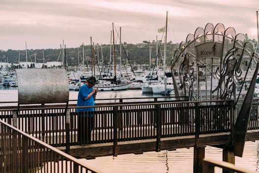 一名男子站在科纳凯码头的木制码头上，身后是游艇和港口