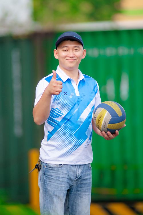 Free East Asian man holding a volleyball and giving a thumbs-up outside. Stock Photo