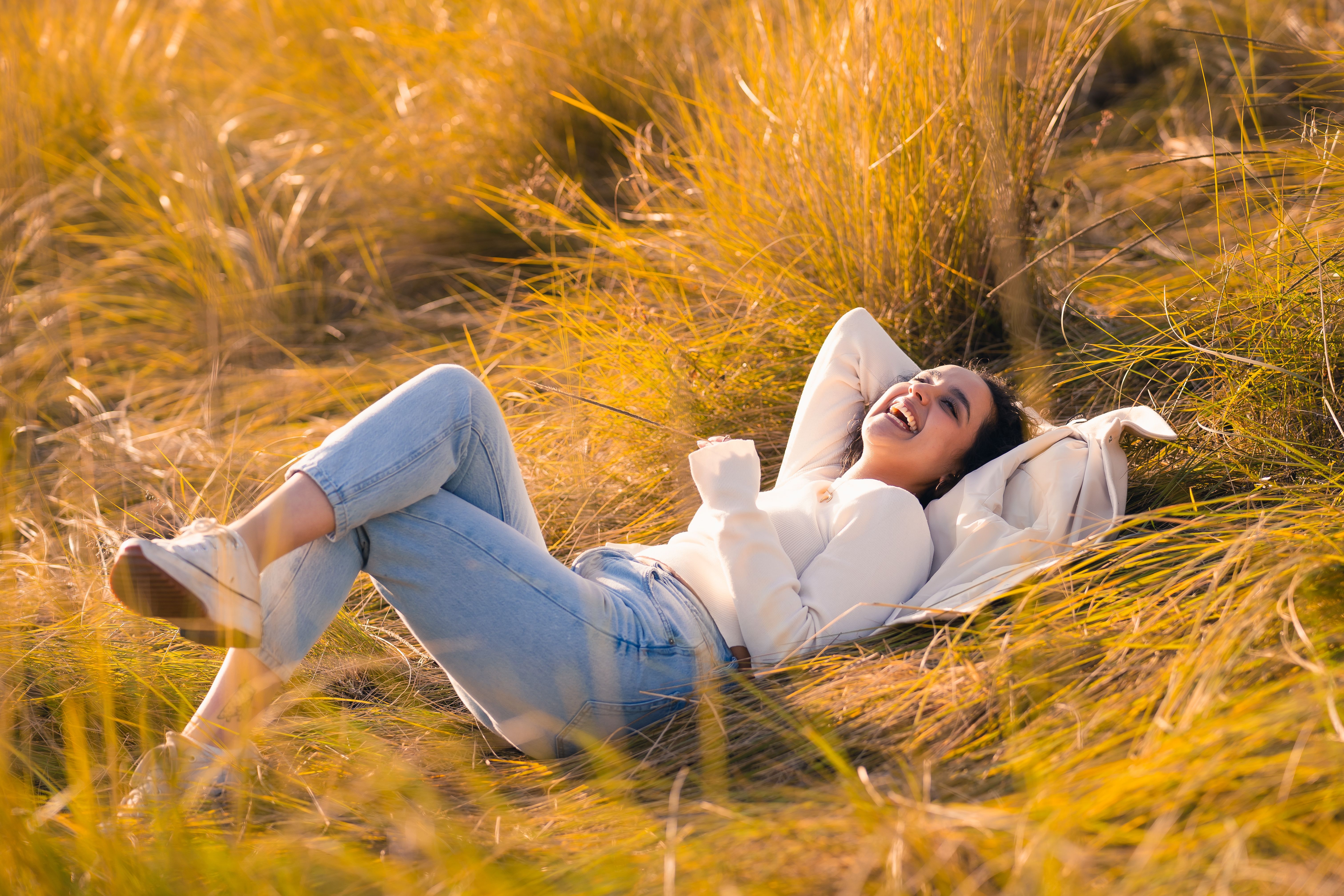 Young woman joyfully relaxing in a sunlit grassfield, embracing nature\'s beauty.