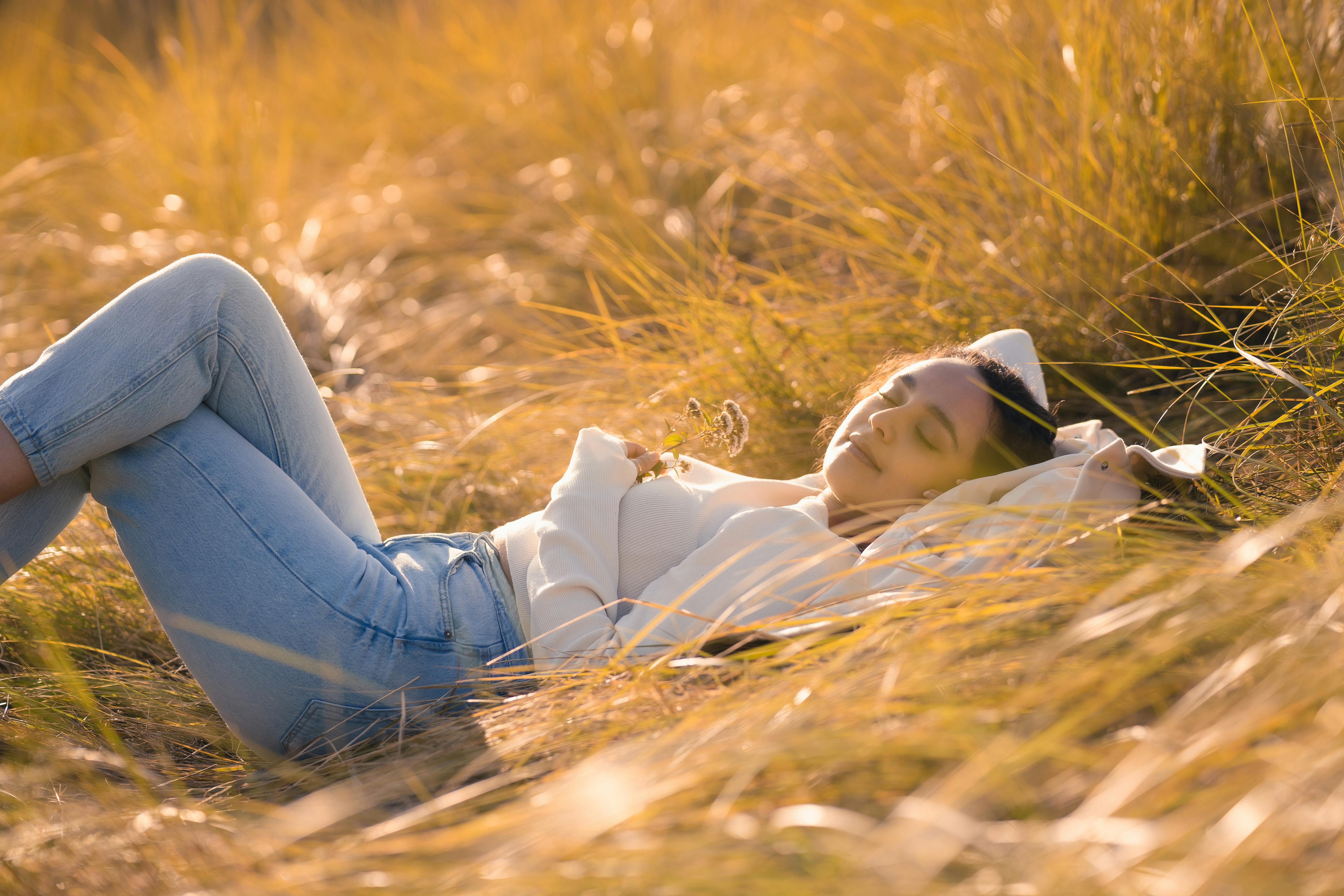 Une jeune femme se repose paisiblement dans un champ ensoleillé d'herbes hautes, embrassant la tranquillité de la nature.
