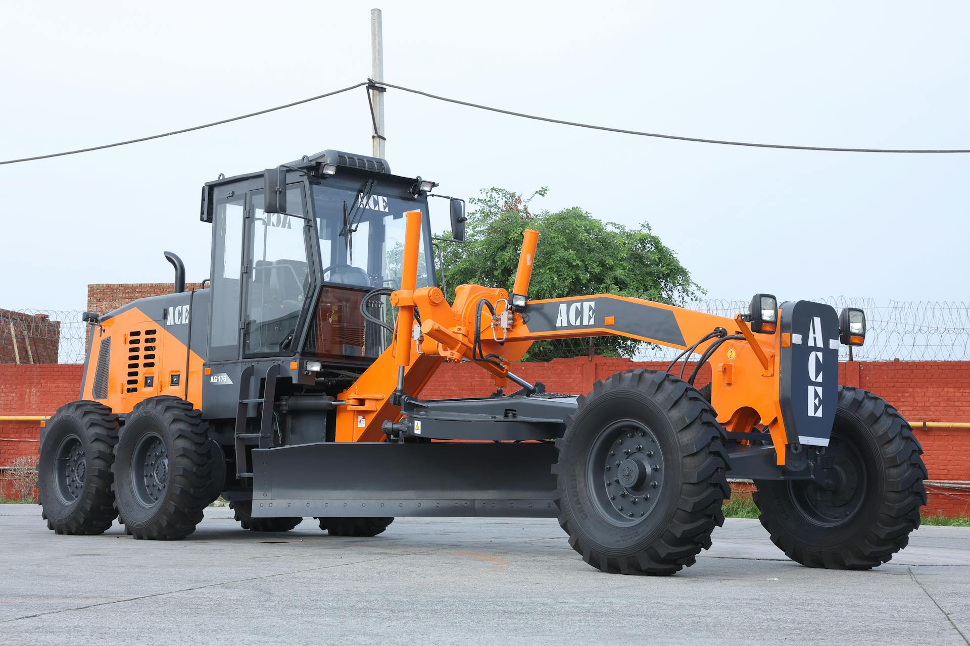 Orange ACE motor grader at road construction site in India, clear day.