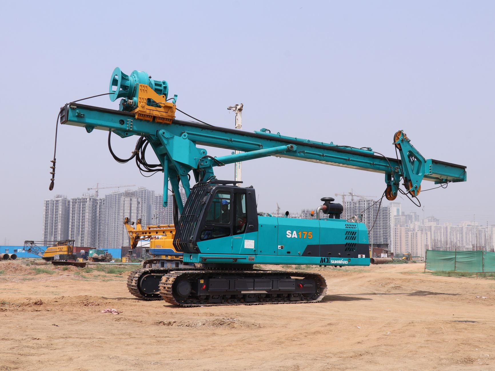 Blue piling rig machine at a construction site in Faridabad, India, with cityscape in background.