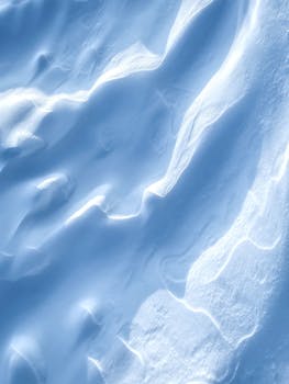 Elegant snow formations create abstract patterns with soft shadows. A serene winter scene with smooth textures.