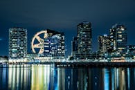 现代城市建筑的倒影在水中呈现出令人惊叹的夜间景观，明亮的摩天轮灯光更凸显了这一点