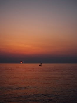 A lone paddler on calm waters during a stunning sunset in Ustica, Sicily. by Manfredi Taglialavoro