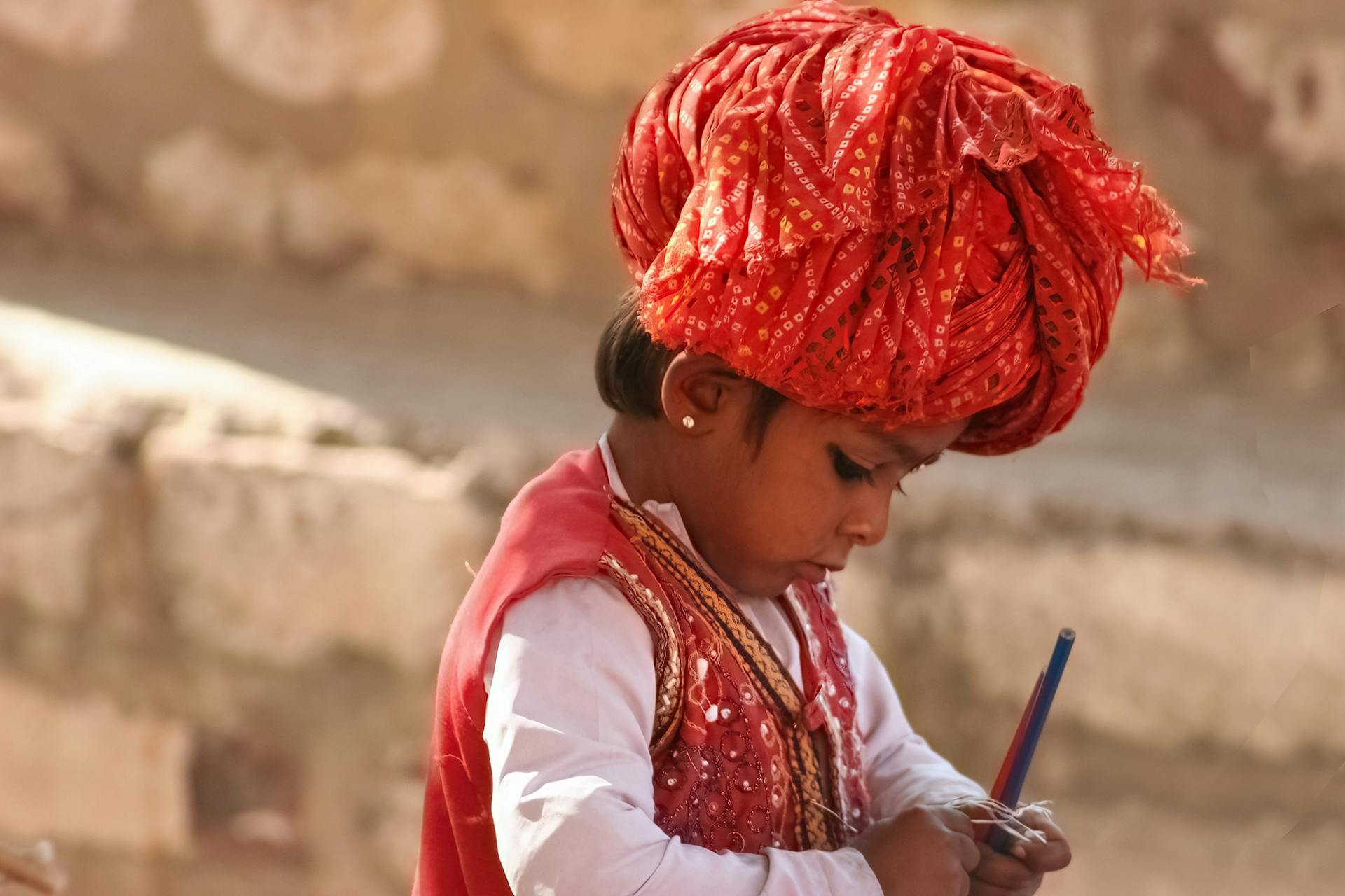 A young child wearing vibrant ethnic attire and a red turban outdoors.