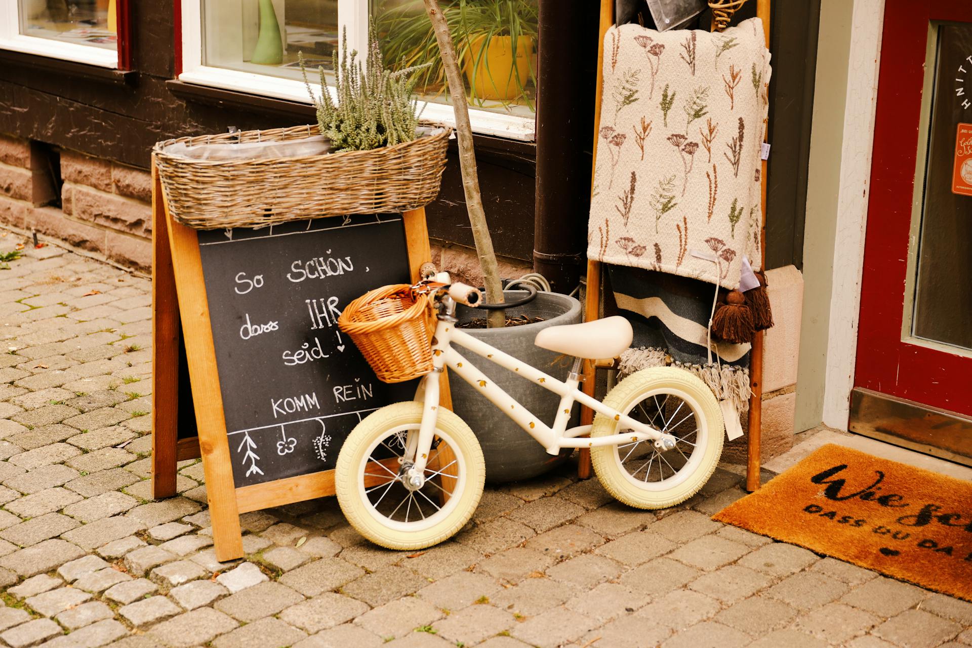 Rustic shopfront with a child's bike, chalkboard sign, and cozy decor in a historic town.