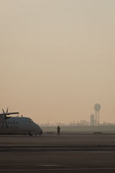 An early morning scene at Schwechat Airport, featuring a solitary figure and aircraft against a hazy sky.