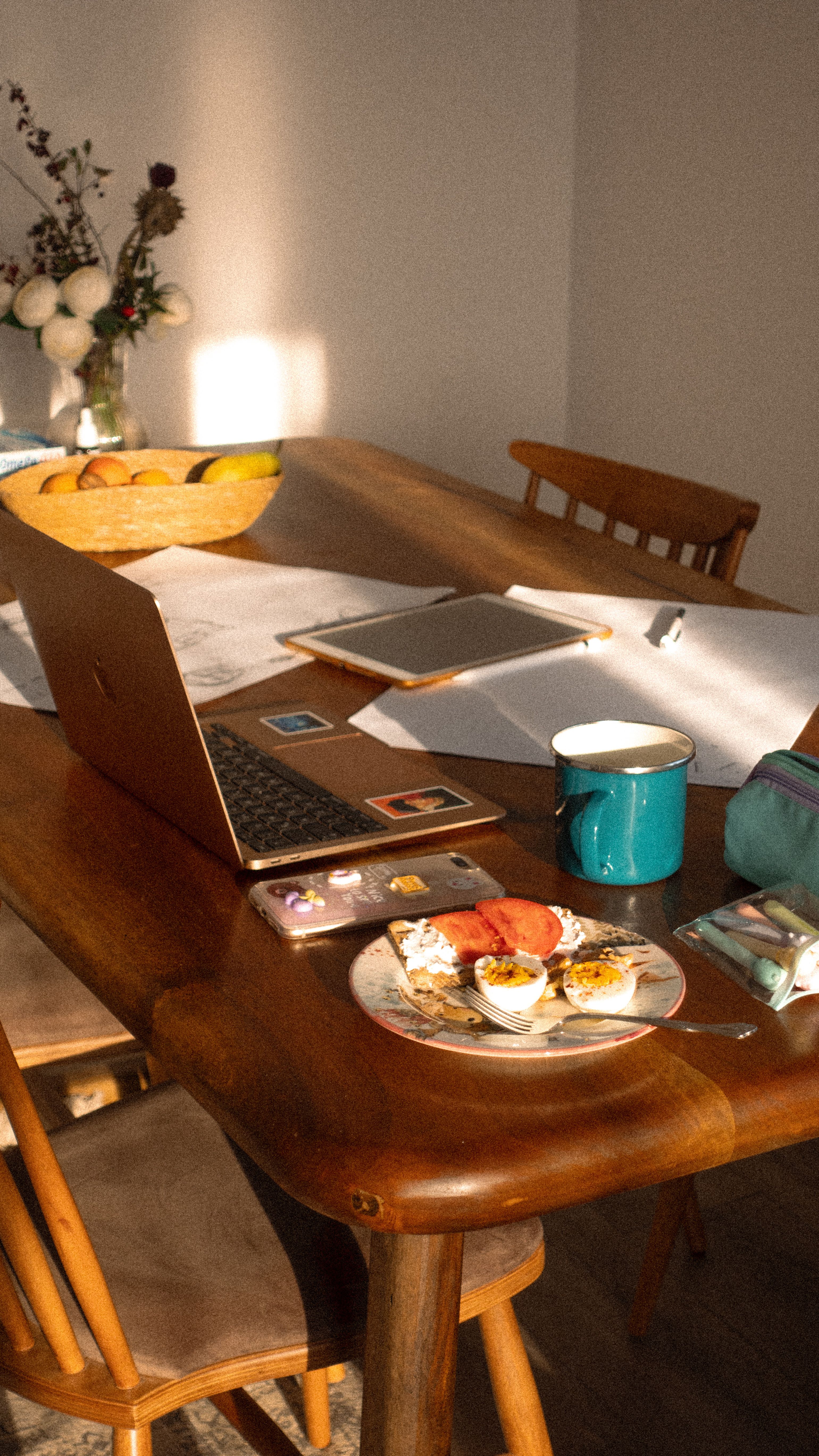 Sunlit wooden table with laptop, notebook, and breakfast, creating a cozy home workspace.