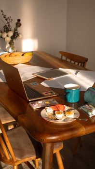 Sunlit wooden table with laptop, notebook, and breakfast, creating a cozy home workspace.