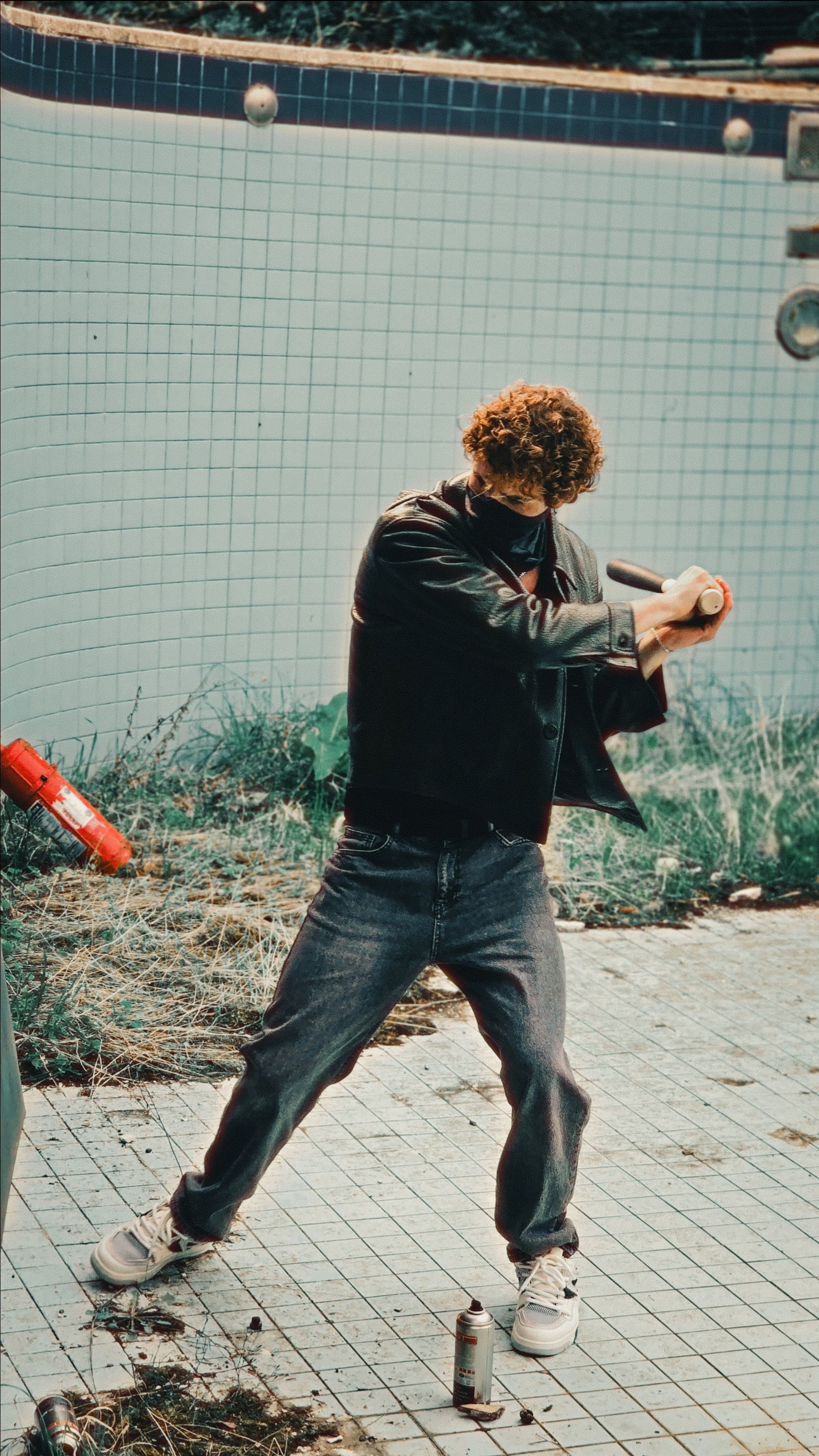 Man smashing a stick in an overgrown, empty swimming pool outdoors. Urban decay theme.
