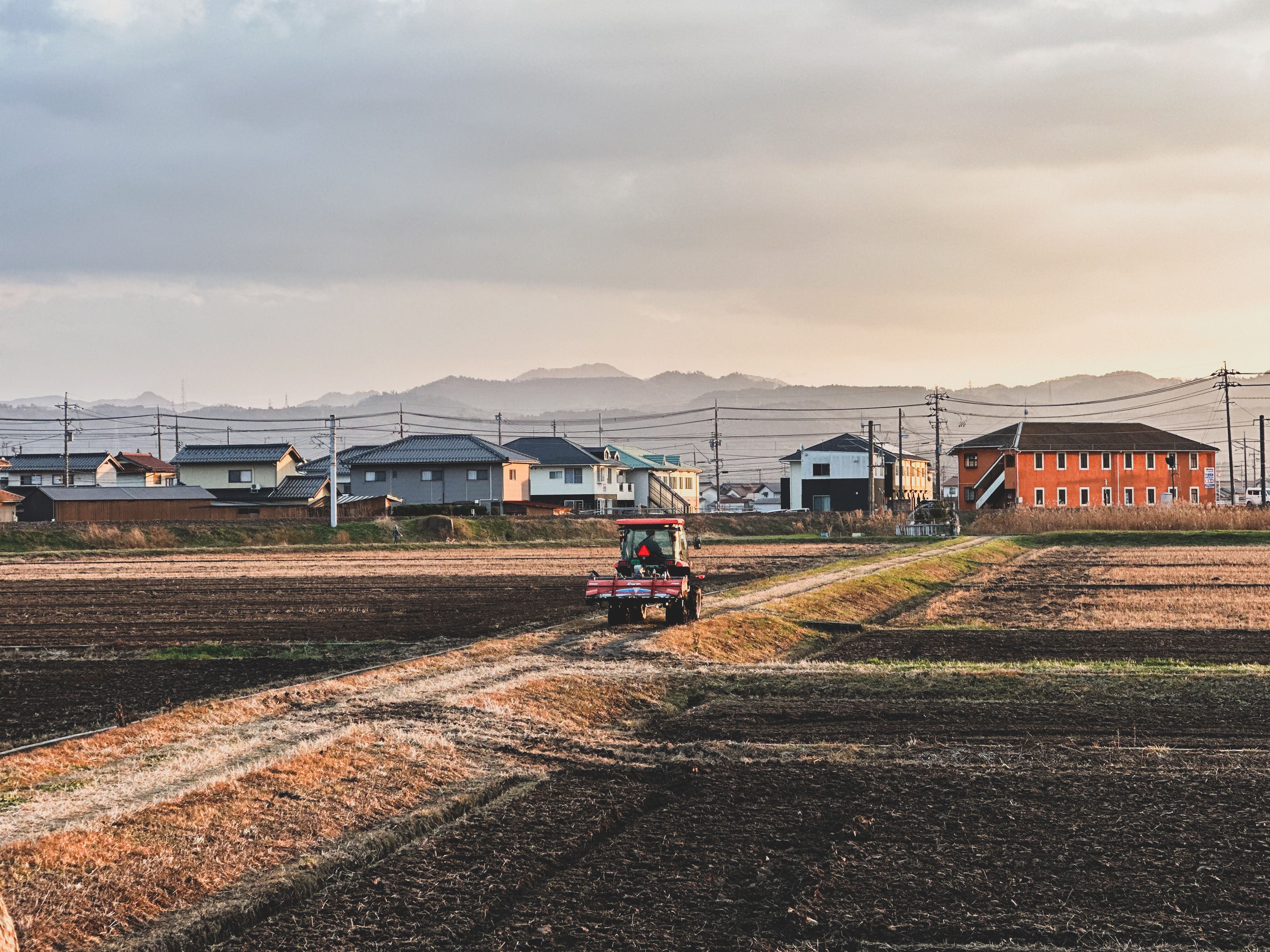 日本の田舎で日没時に、家々を背景に畑を耕すトラクター。