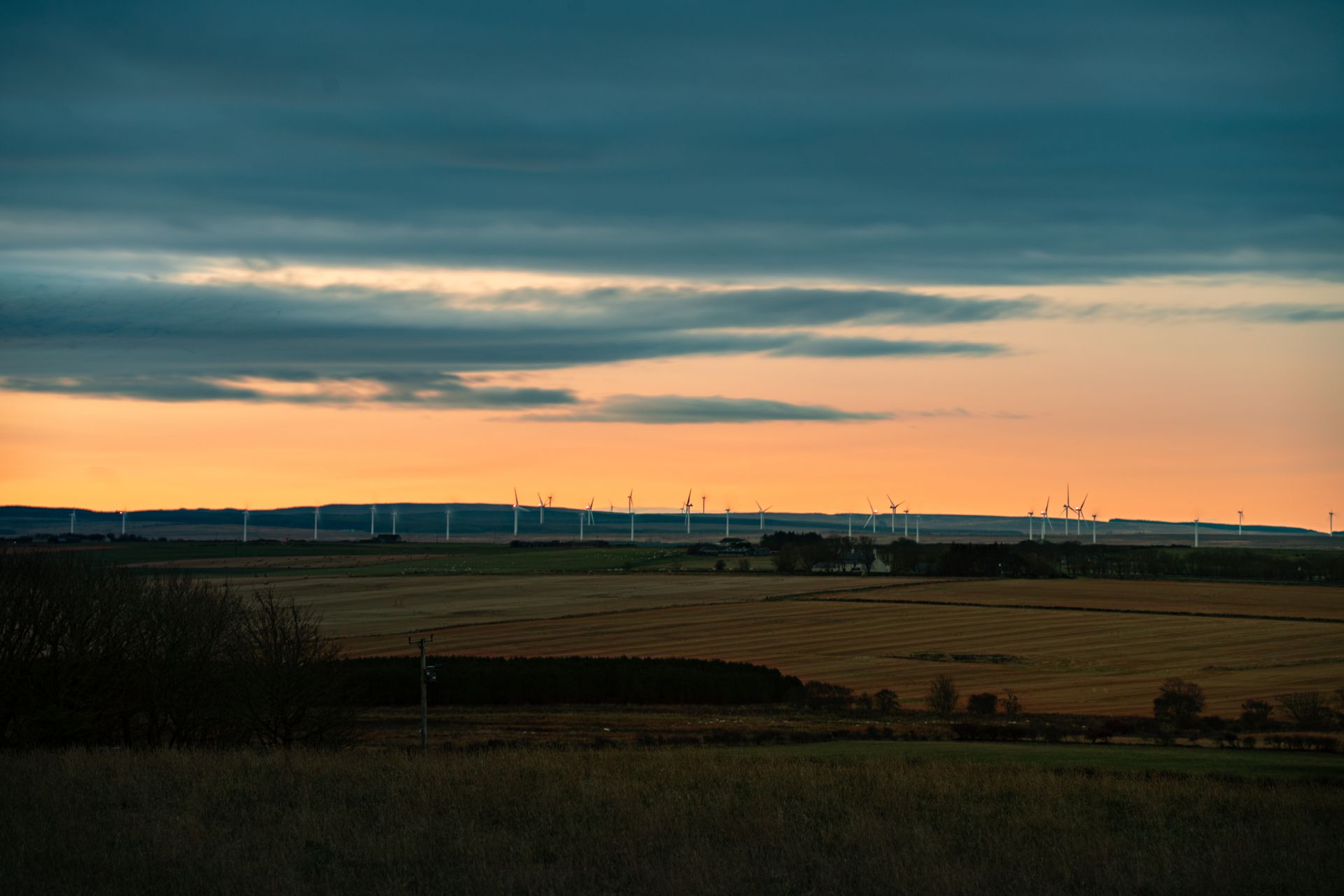 A serene landscape featuring wind turbines under a dramatic sunset sky, ideal for renewable energy themes.