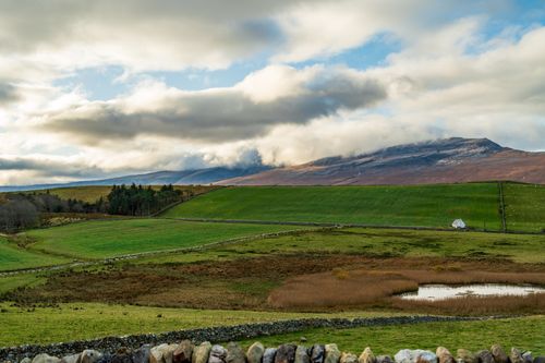 Free Peaceful landscape with green fields, distant mountains, and dramatic clouds. Stock Photo