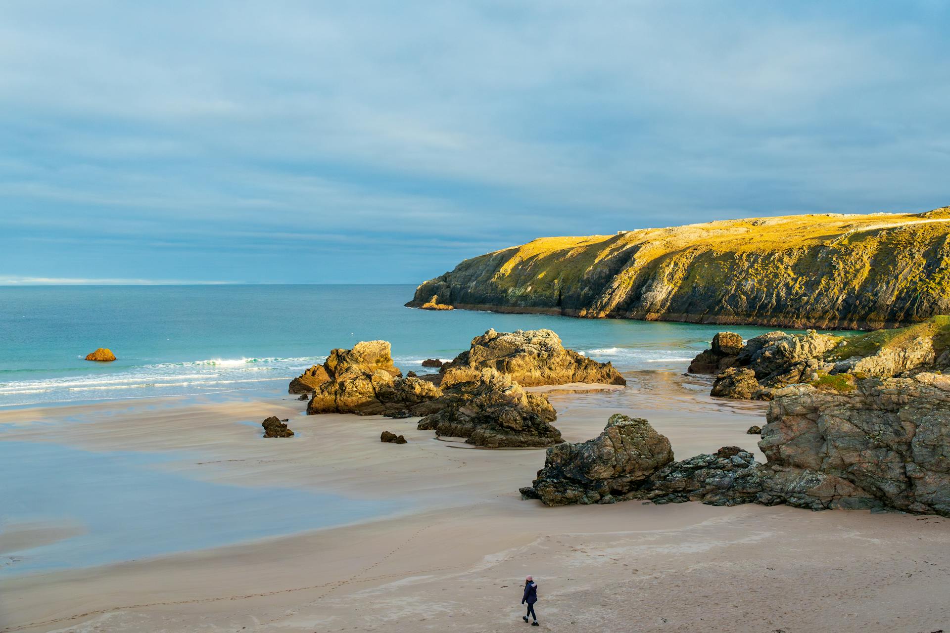 Discover the serenity of a rocky beach with dramatic cliffs and azure waters under a bright sky.