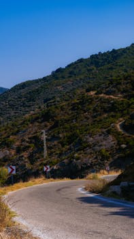 A picturesque curvy mountain road meanders through lush greenery under a clear blue sky, ideal for travel and nature enthusiasts.