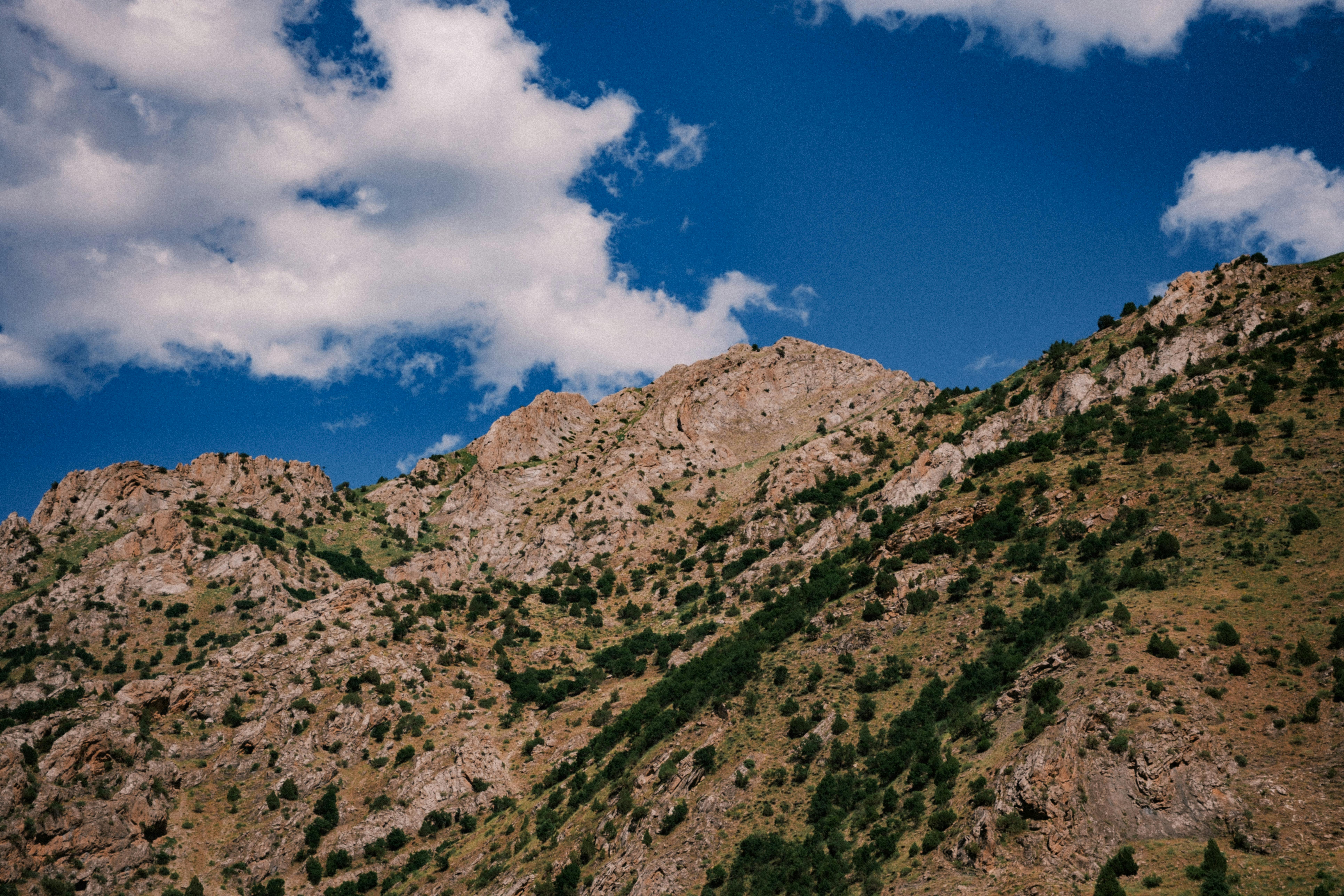 High-altitude rocky mountain slope under a bright blue sky with clouds.