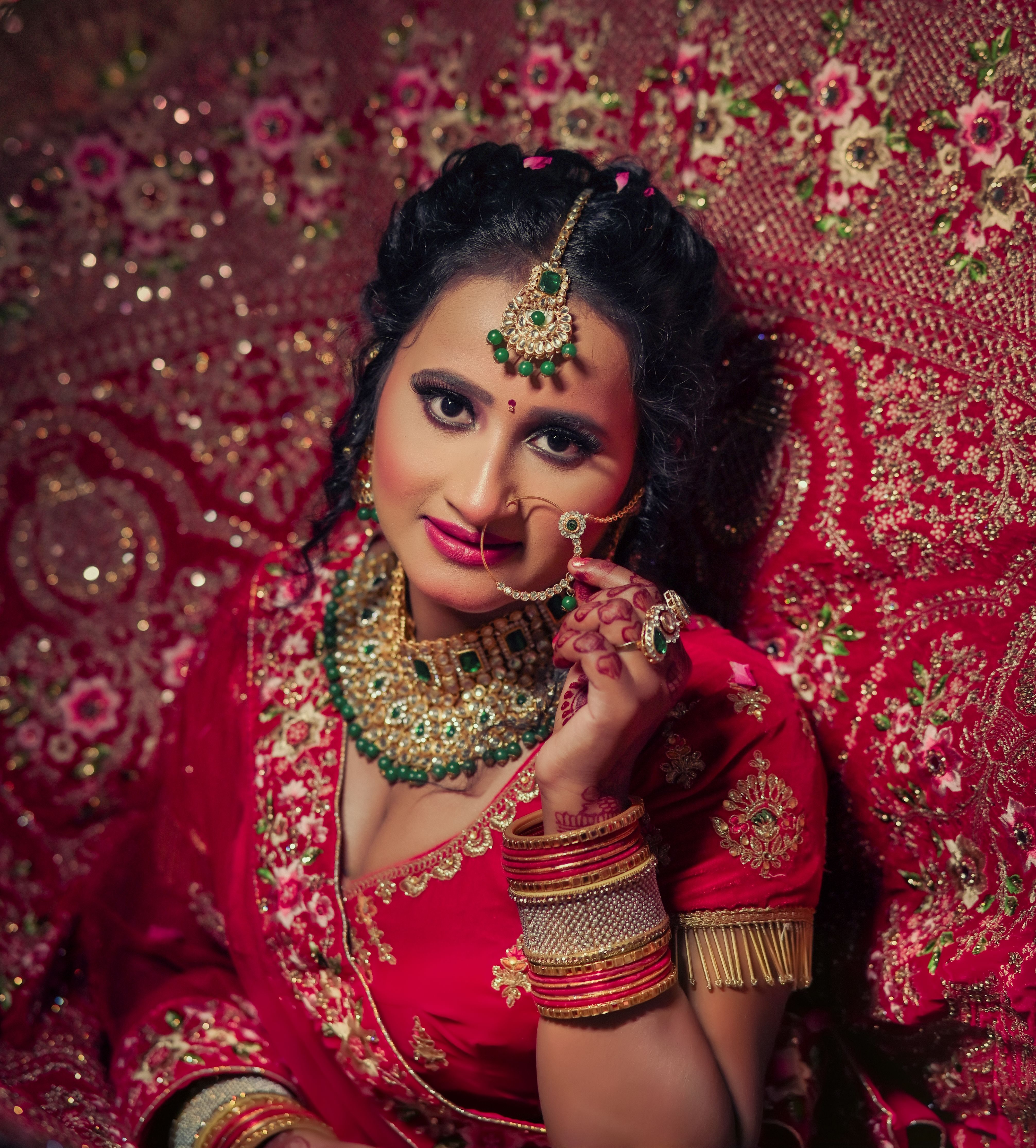 Stunning Indian bride in vibrant red saree, adorned with intricate jewelry, showcasing cultural elegance indoors.