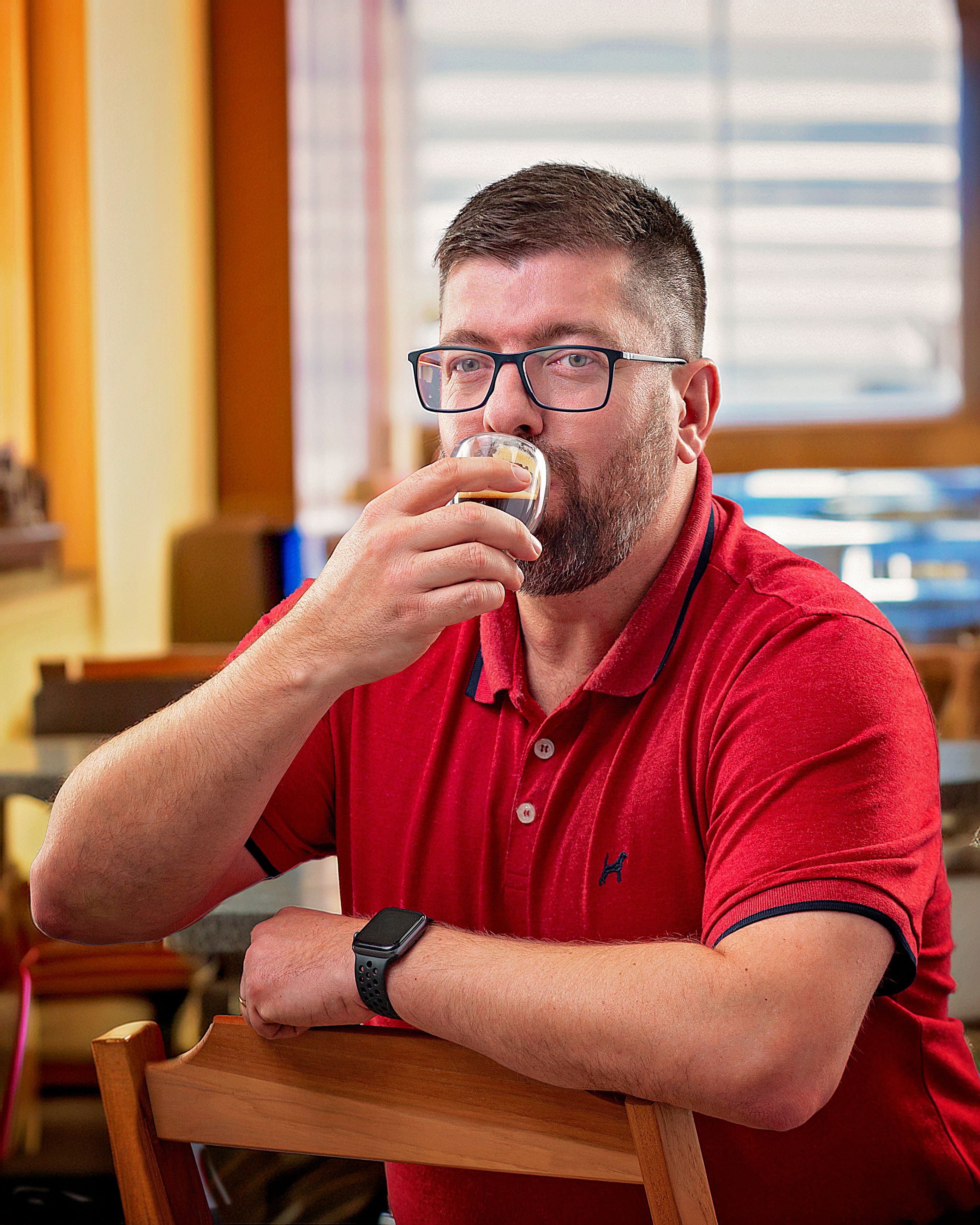 A man in a red shirt savors a beverage indoors at a cozy cafe setting.