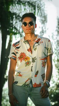 Stylish young man wearing a floral shirt and sunglasses, posing confidently outdoors.