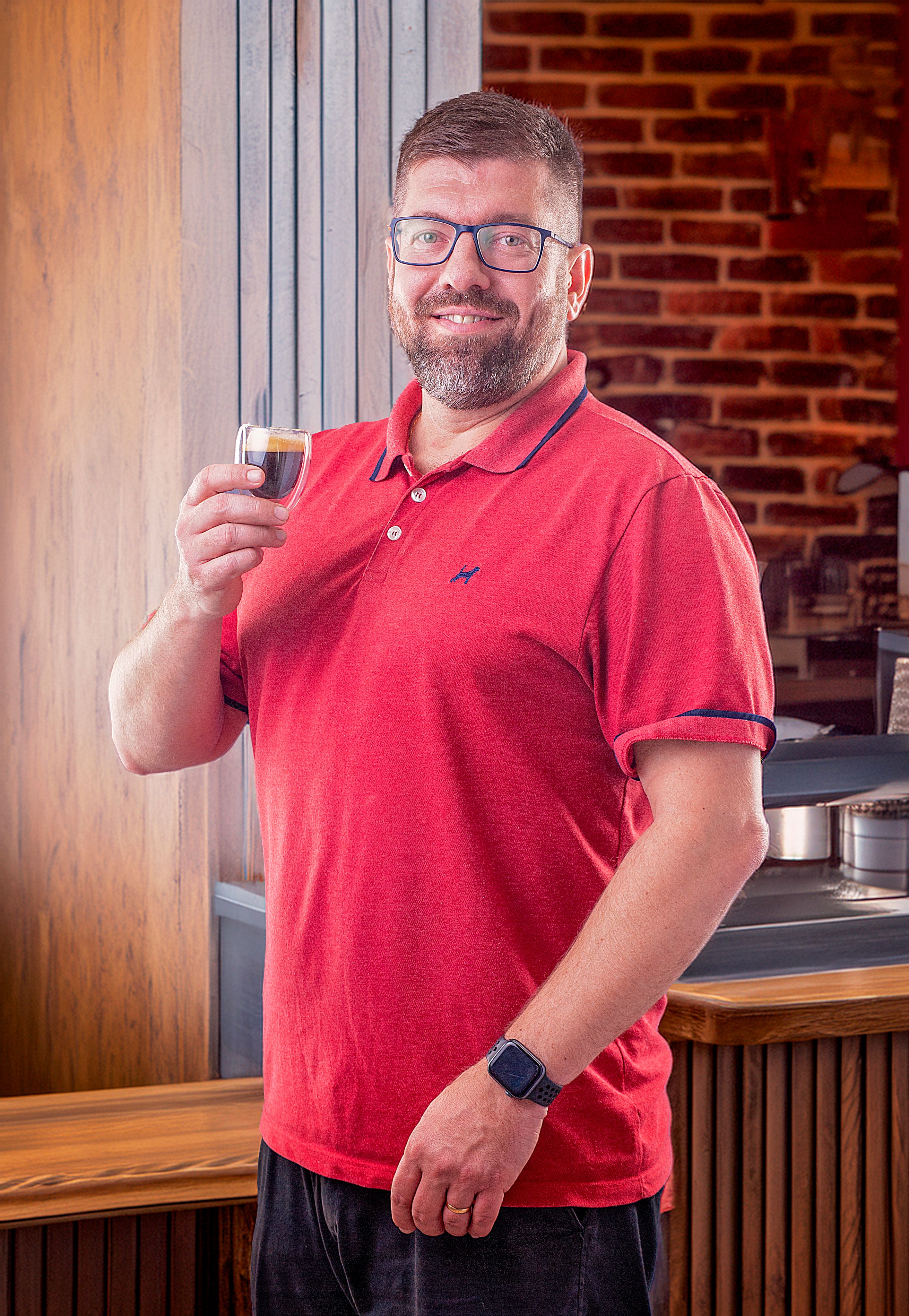 Smiling man holding espresso in a cozy café with brick interior.