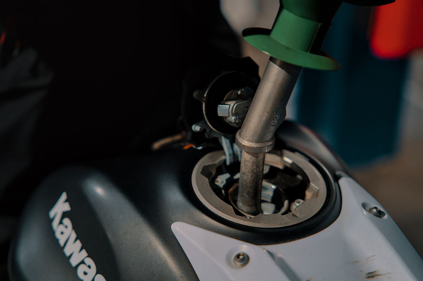 Close-up of refueling a Kawasaki motorcycle at a gas station, with nozzle inserted into the tank.