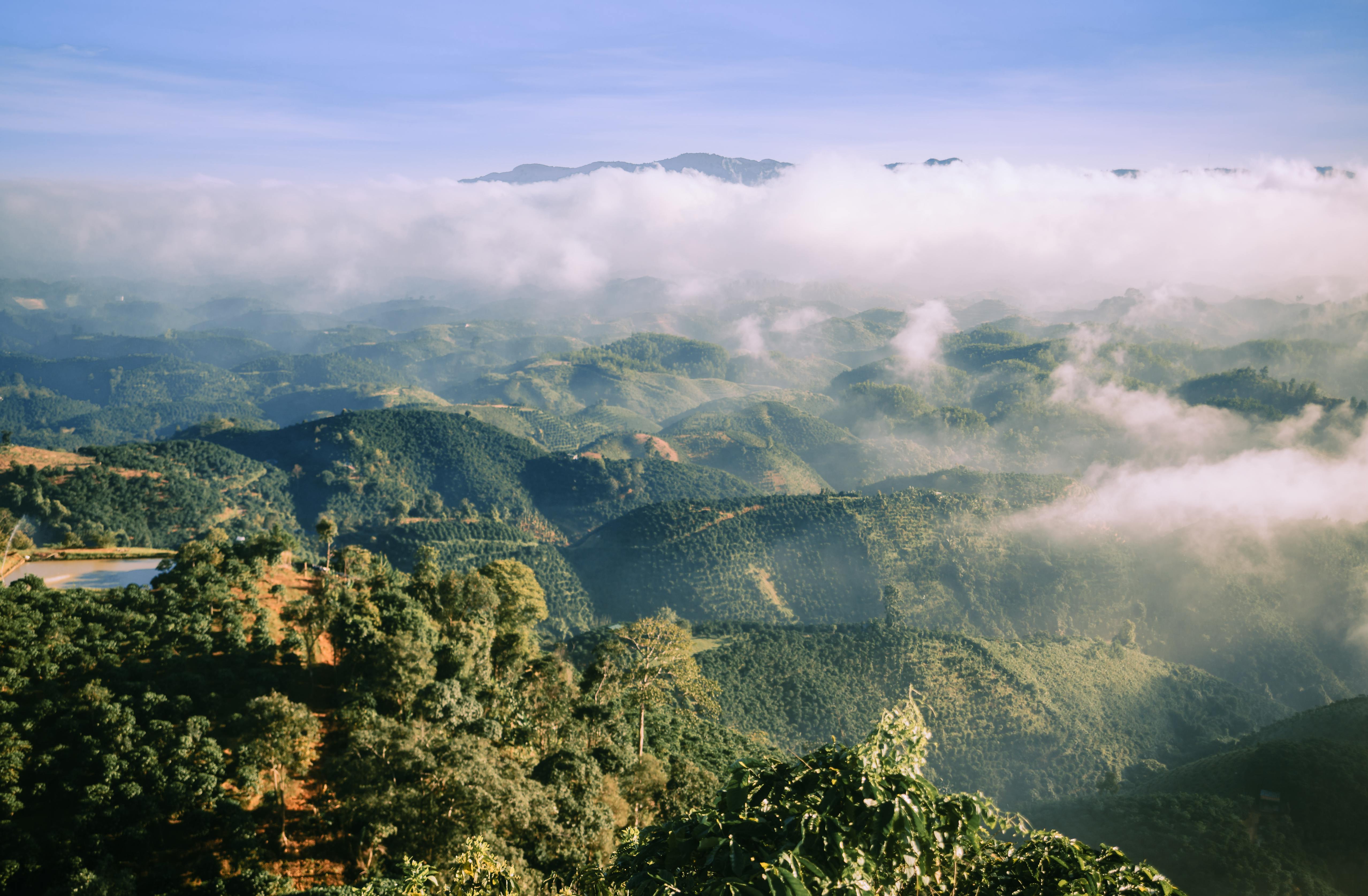 Aerial view of green mountains and clouds on a clear day, showcasing natural beauty.