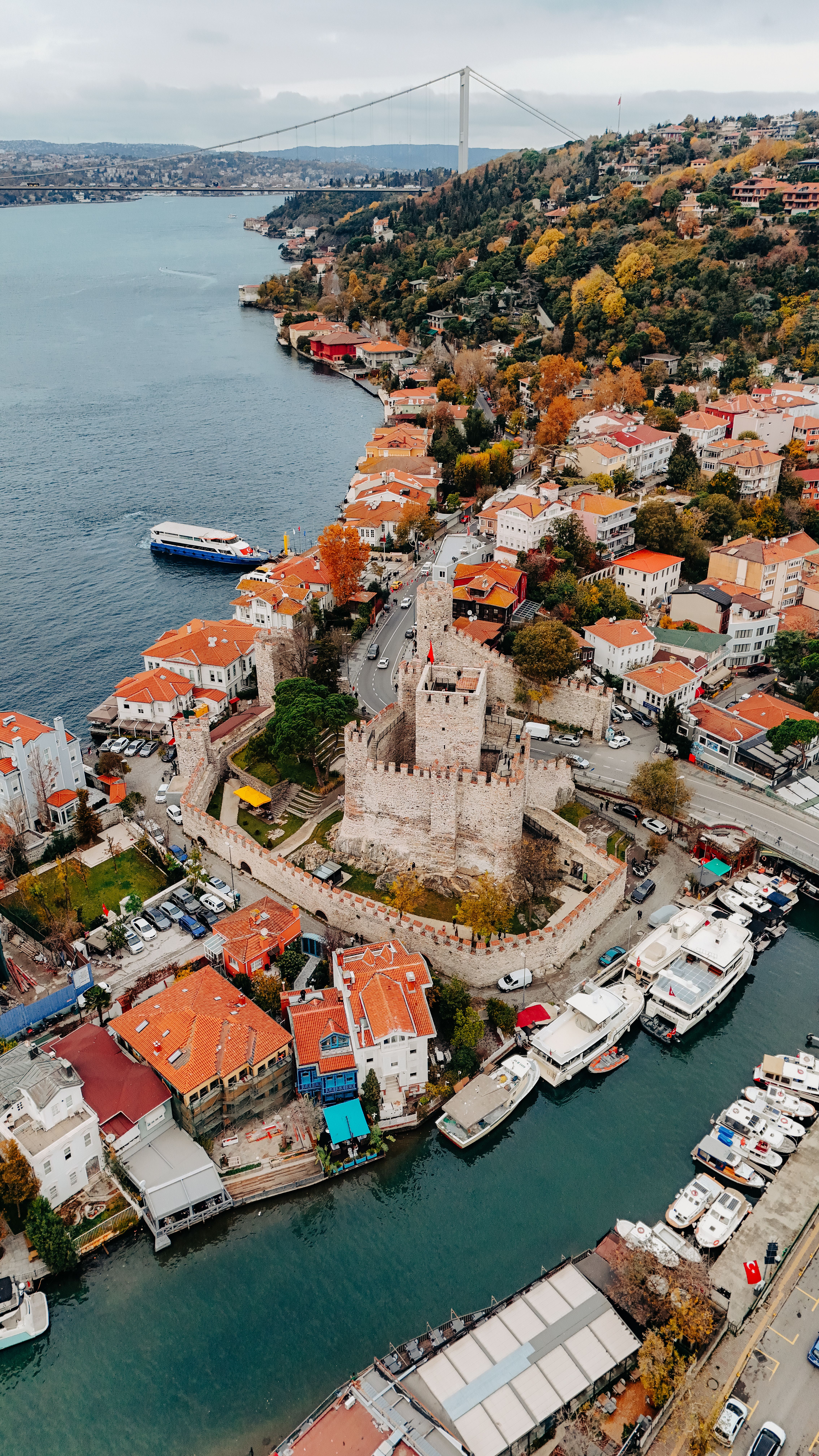 Aerial shot of Anadolu Hisarı and Bosphorus in Istanbul with vibrant autumn foliage.