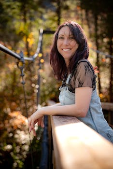 A cheerful woman enjoying a sunny autumn day on a suspension bridge surrounded by fall foliage.