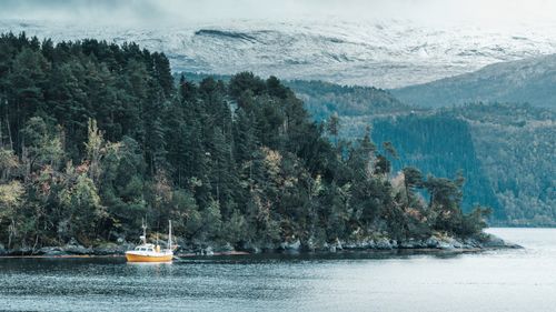 Free Yellow fishing boat in scenic Norwegian fjord with snow-covered mountains and forests. Stock Photo