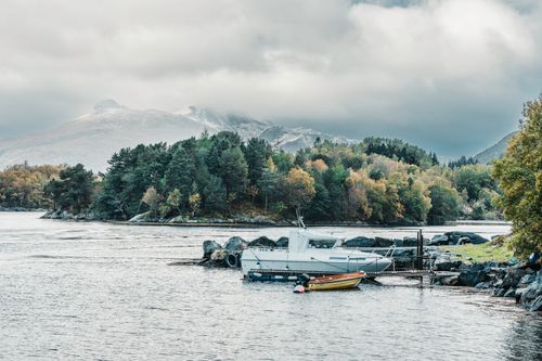 Free Tranquil scene of boats by a Norwegian lake with snow-covered mountains in autumn. Stock Photo