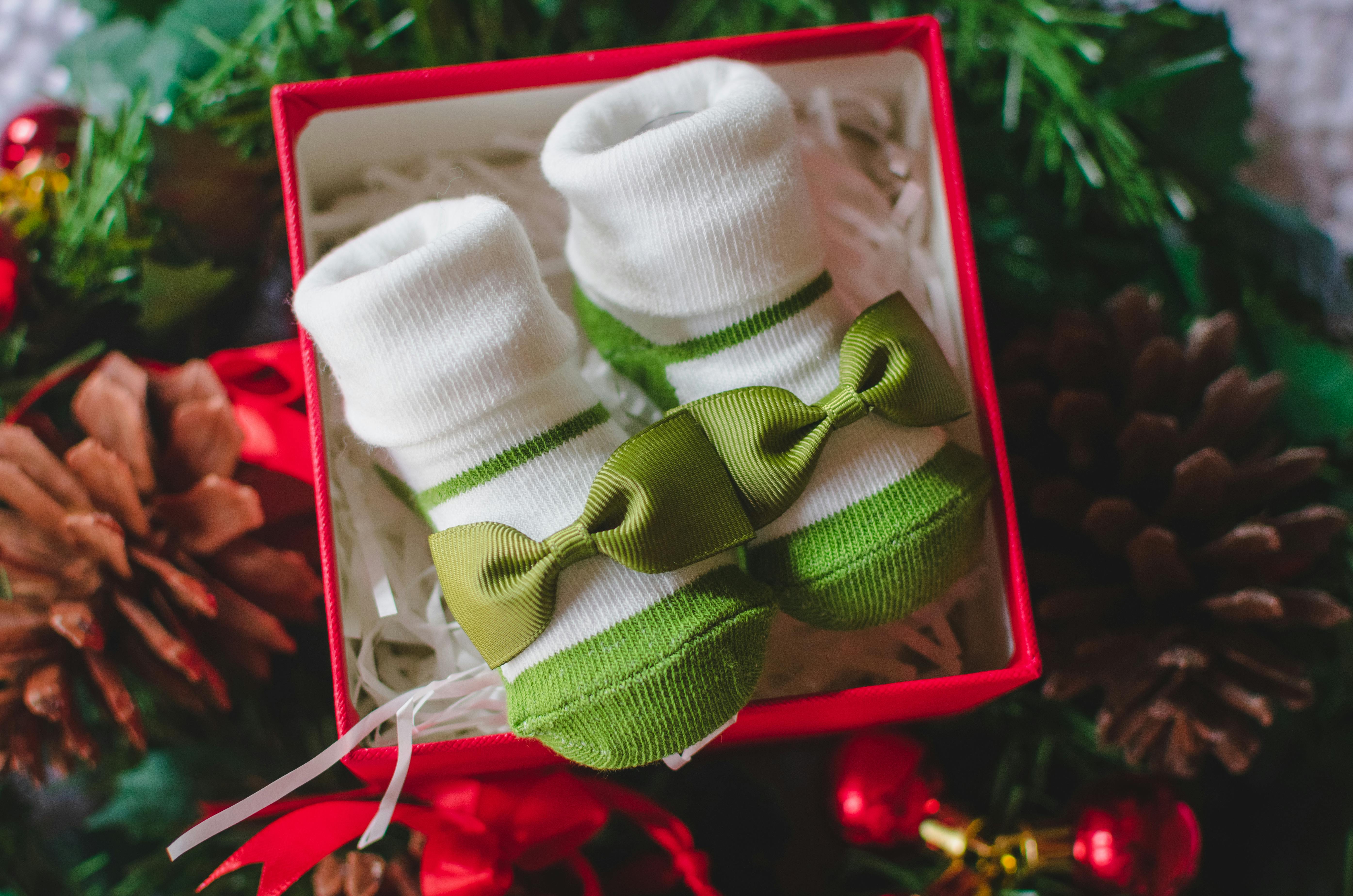 Adorable baby socks with bows in a Christmas-themed gift box surrounded by festive decor.