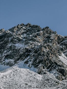 A majestic snow-covered mountain peak under a clear blue sky, showcasing rugged natural beauty.