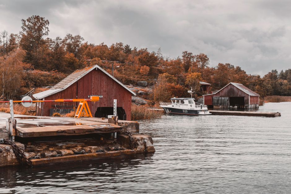 Picturesque autumn harbor scene with boat sheds and a ferry station in the Åland Islands.