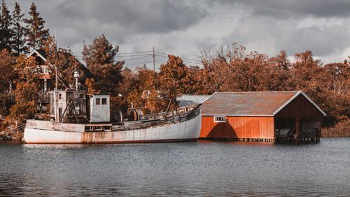 Free An old fishing boat docked by a colorful autumn forest and red shed by the water. Stock Photo
