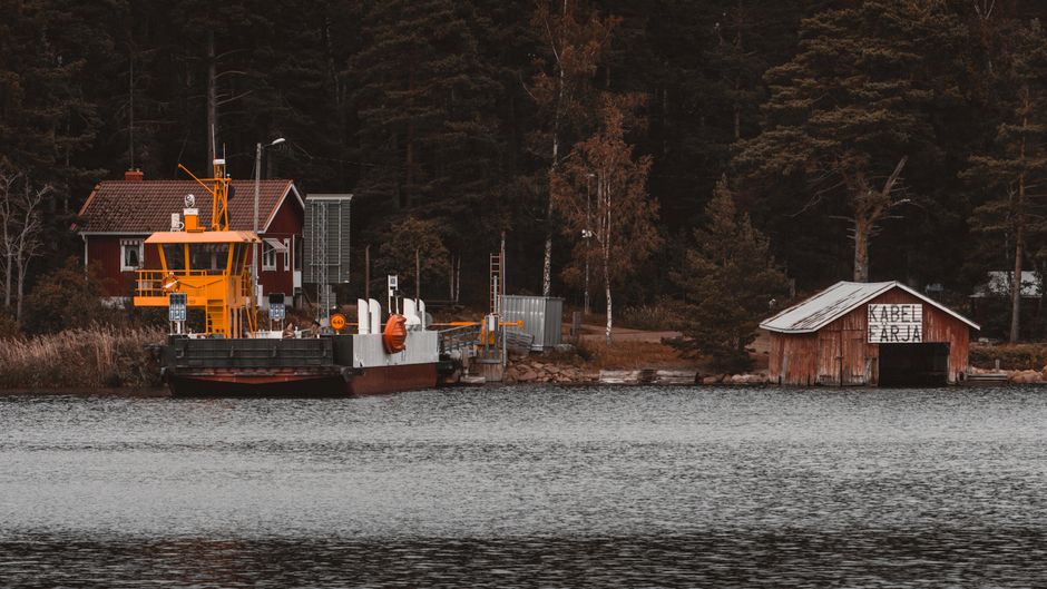 A serene boat shed by a ferry station in the Åland Islands, Finland, surrounded by dense forest.
