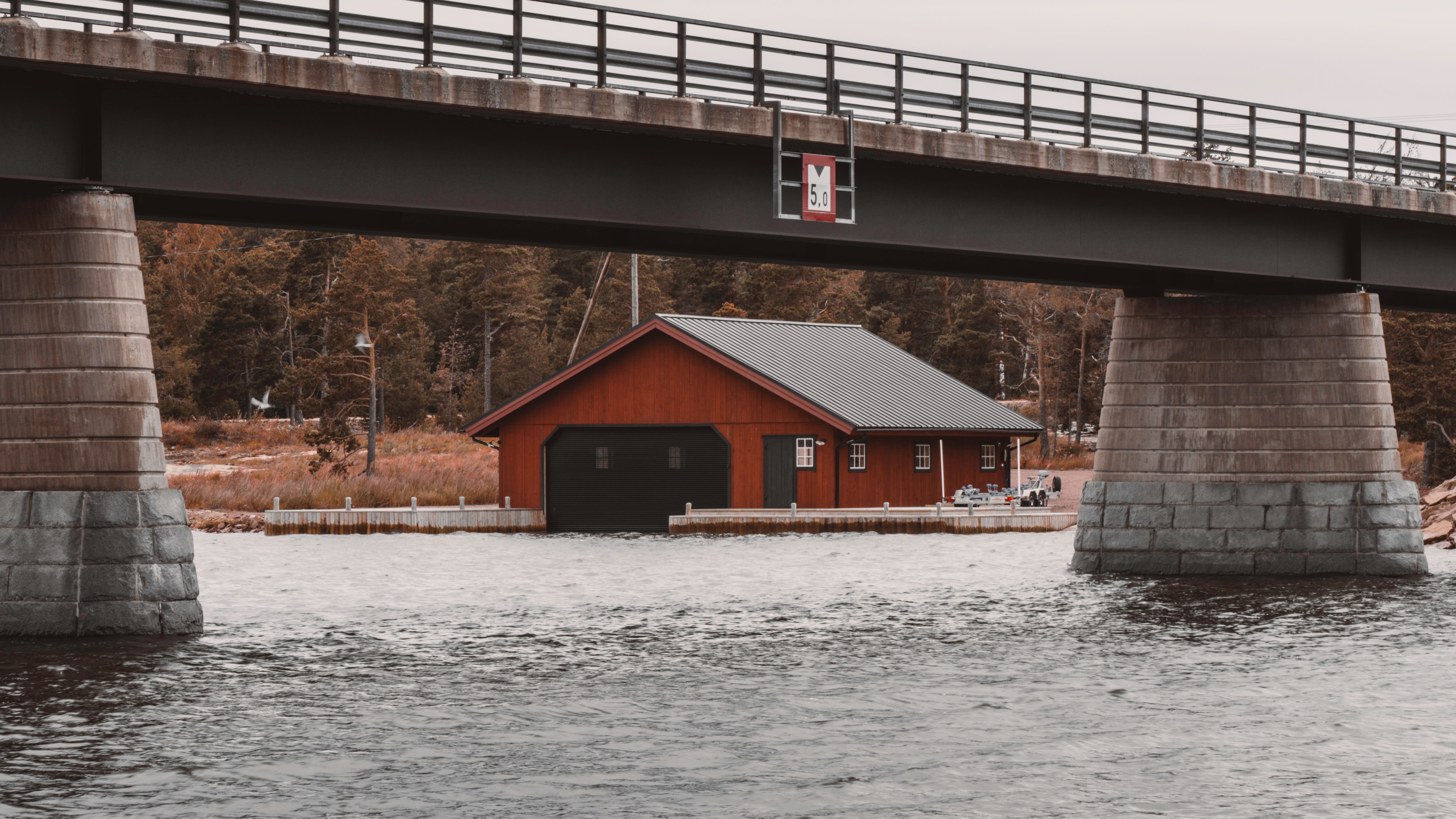 Picturesque view of a red boat shed nestled under a bridge in Åland Islands, Finland.