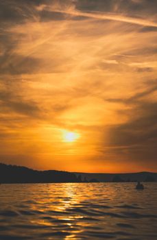 A serene sunset over a calm lake with a golden sky and silhouetted hills.