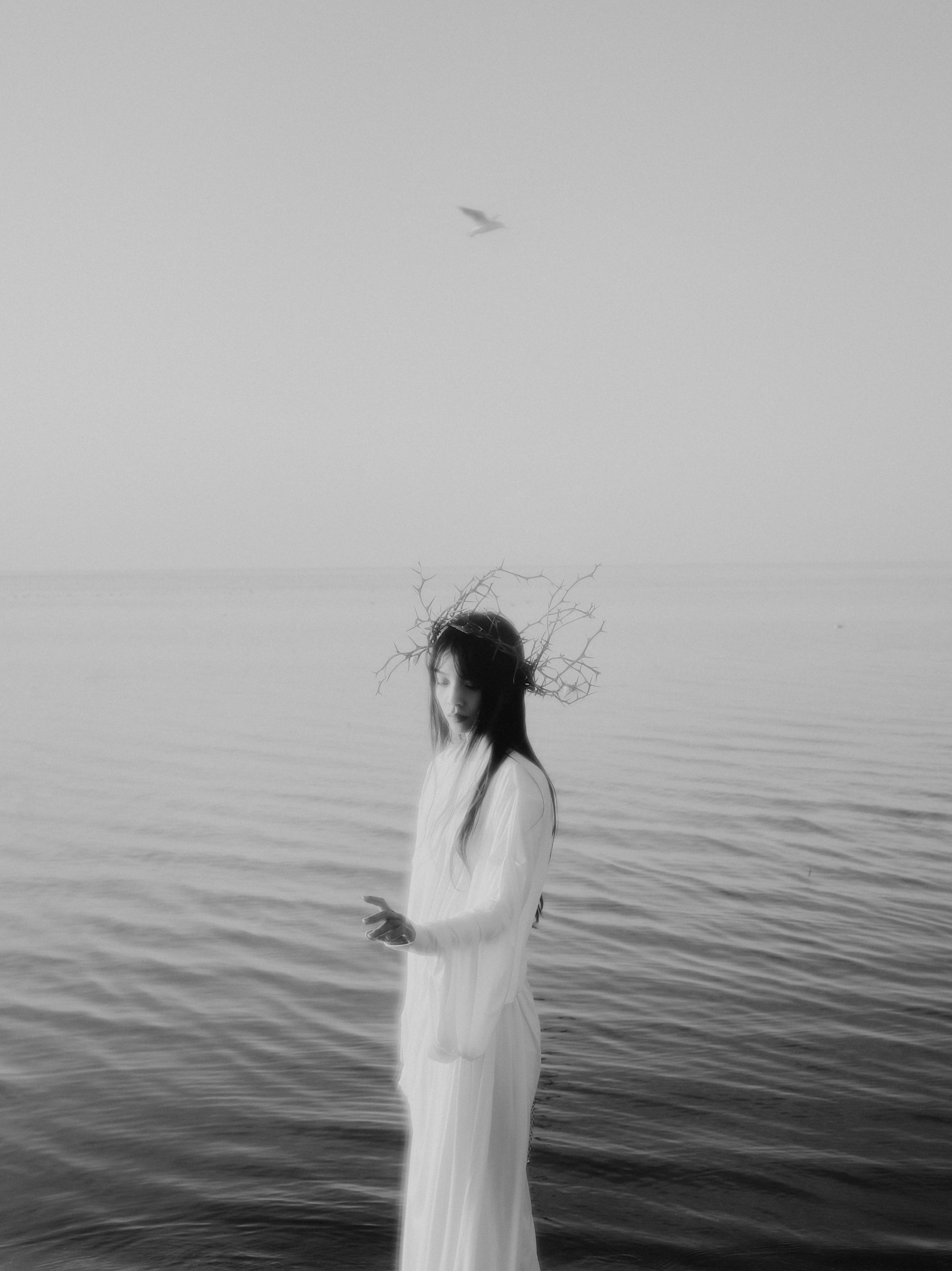 Artistic black and white photo of a woman in a gown by the sea with a dreamy atmosphere.
