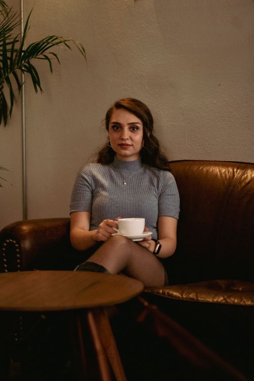 Free A young woman sitting comfortably in a cozy cafe, savoring a warm cup of coffee. Stock Photo