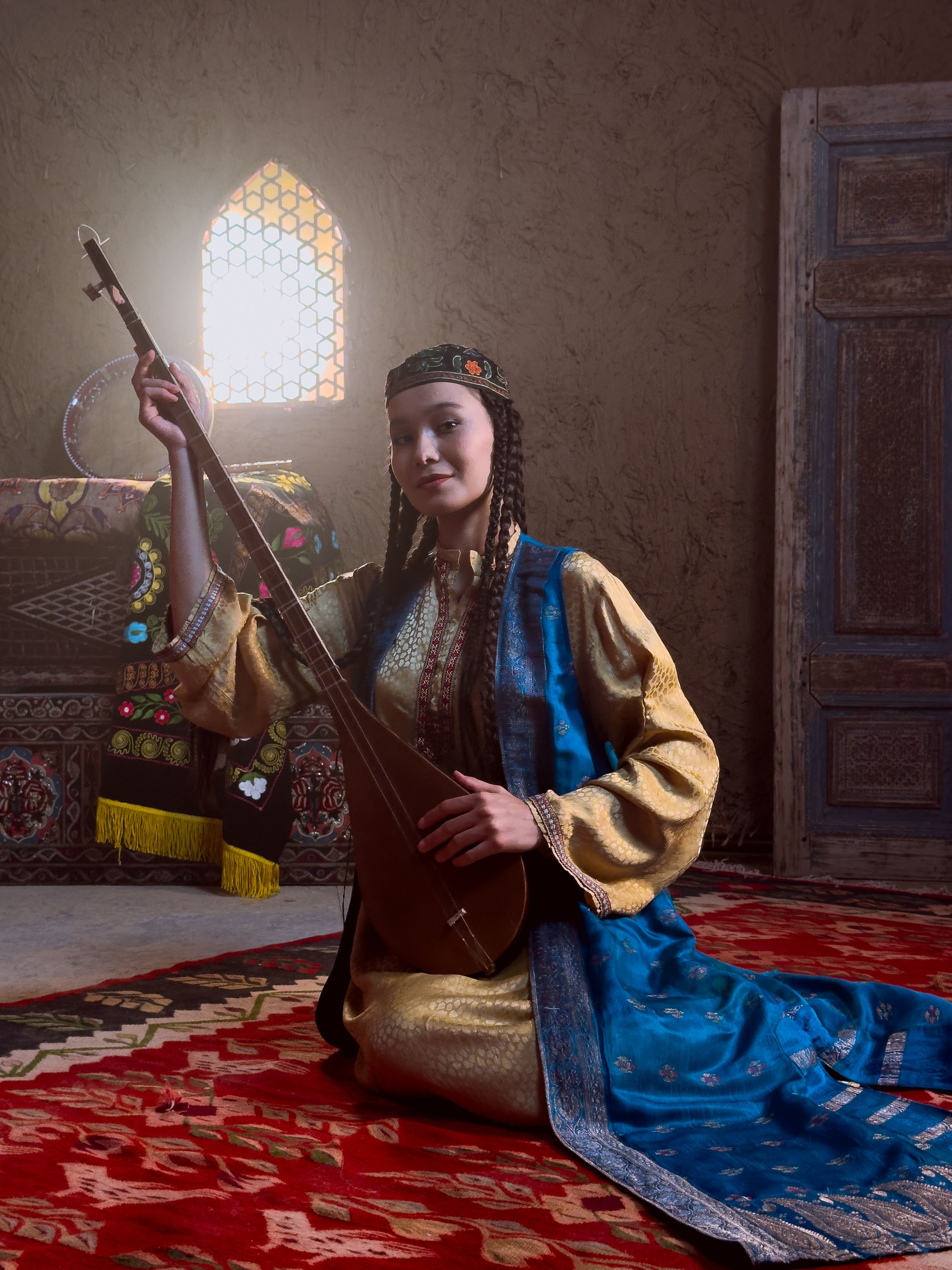Woman in traditional attire playing a Central Asian lute inside a decorated room.