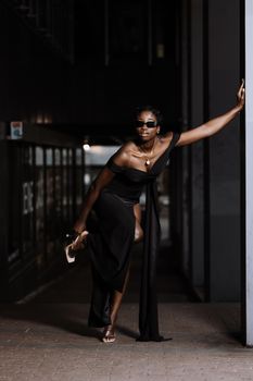 Stylish woman in a black dress posing elegantly against a dark background indoors.